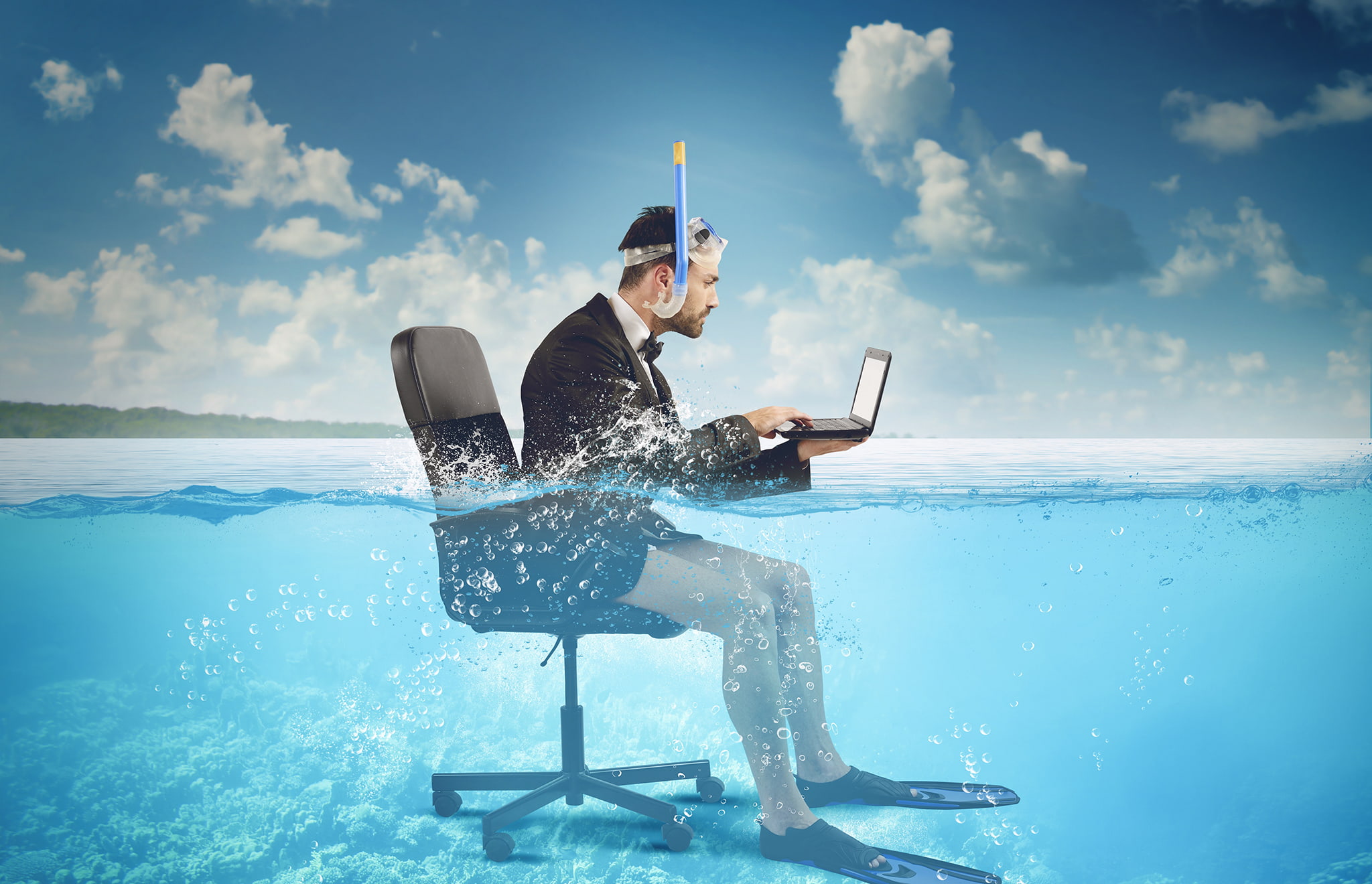 Man sat on a desk chair on his laptop in the sea.