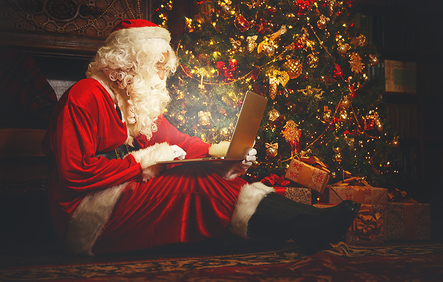Santa sat in front of a tree on a laptop.