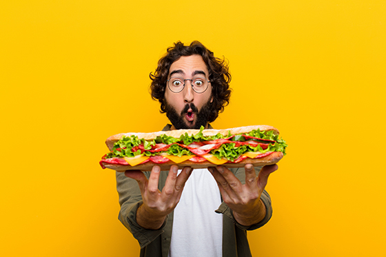 Man holding a giant sandwich looking shocked.