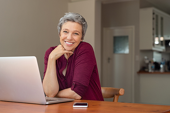 Old woman smiling behind a laptop.