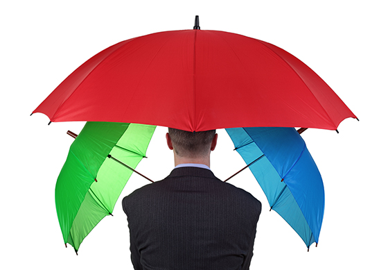 Man in a suit holding three different coloured umbrellas.