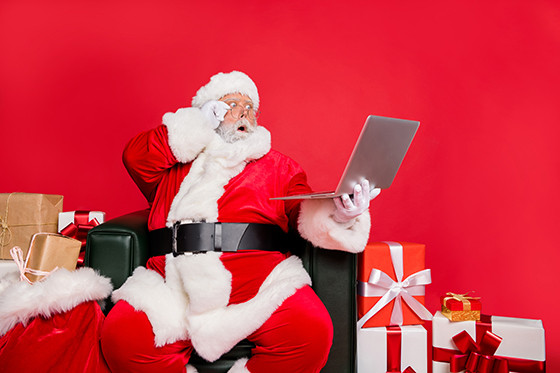 Santa sat on a chair, holding a laptop, looking shocked.