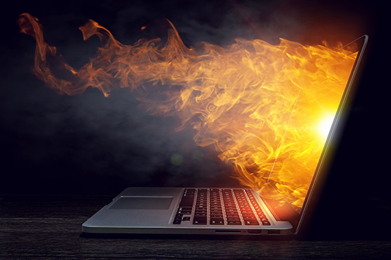 Laptop in fire flames on dark background.