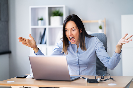 Woman expressing anger and waving her hands at her laptop.