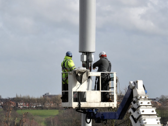 Two engineers on a crane fixing a telecoms tower.